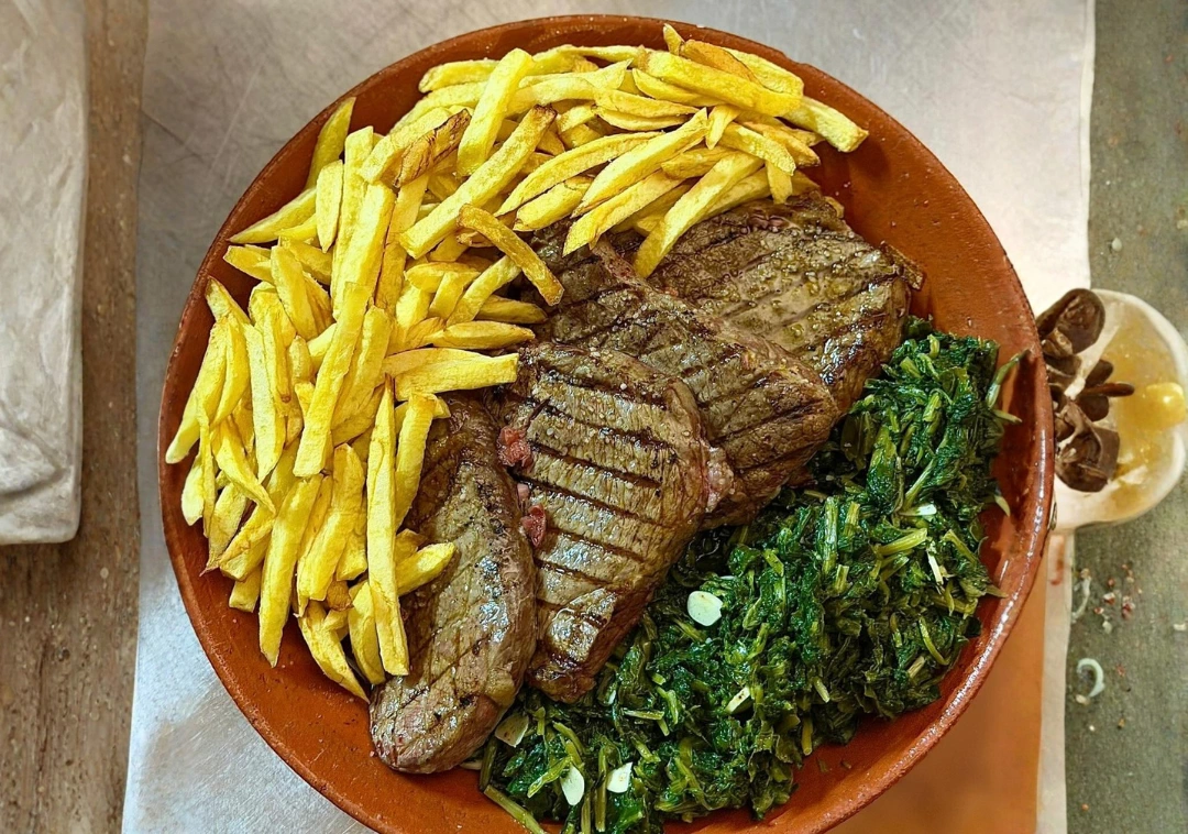 Posta de vitela grelhada com batata frita e grelos, em travessa de barro